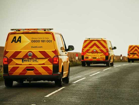 Three yellow AA patrol vans drive down a remote country road