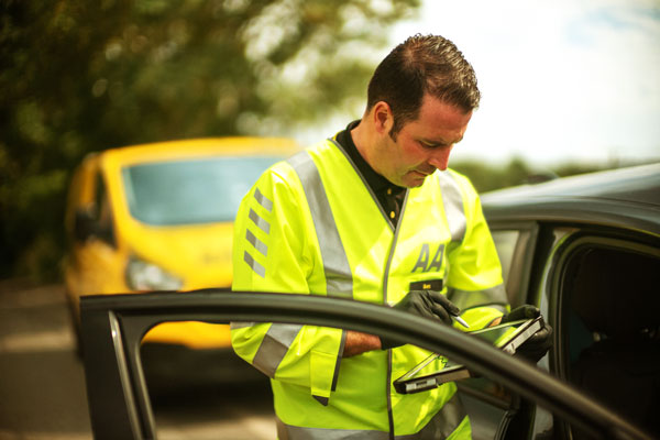 An AA patrol checks his device while attending a breakdown