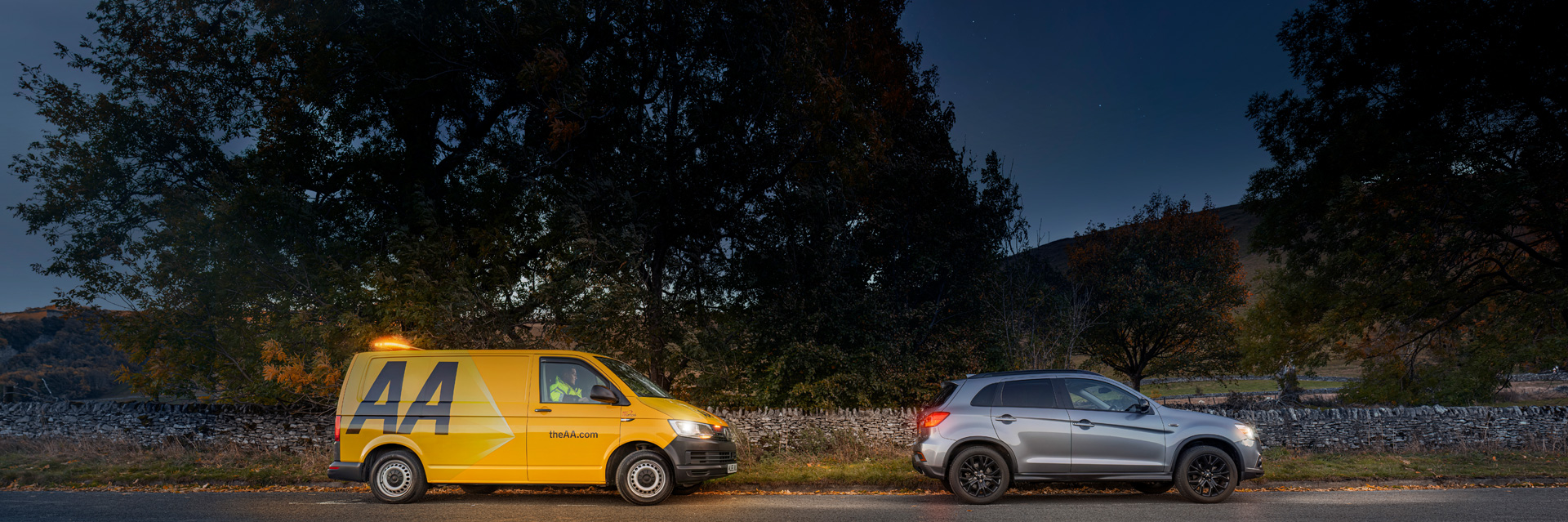 A yellow AA patrol van and silver car on side of road